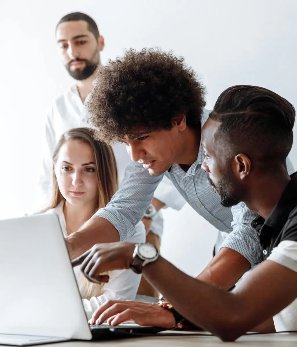Diverse team collaborating and discussing work around a laptop.